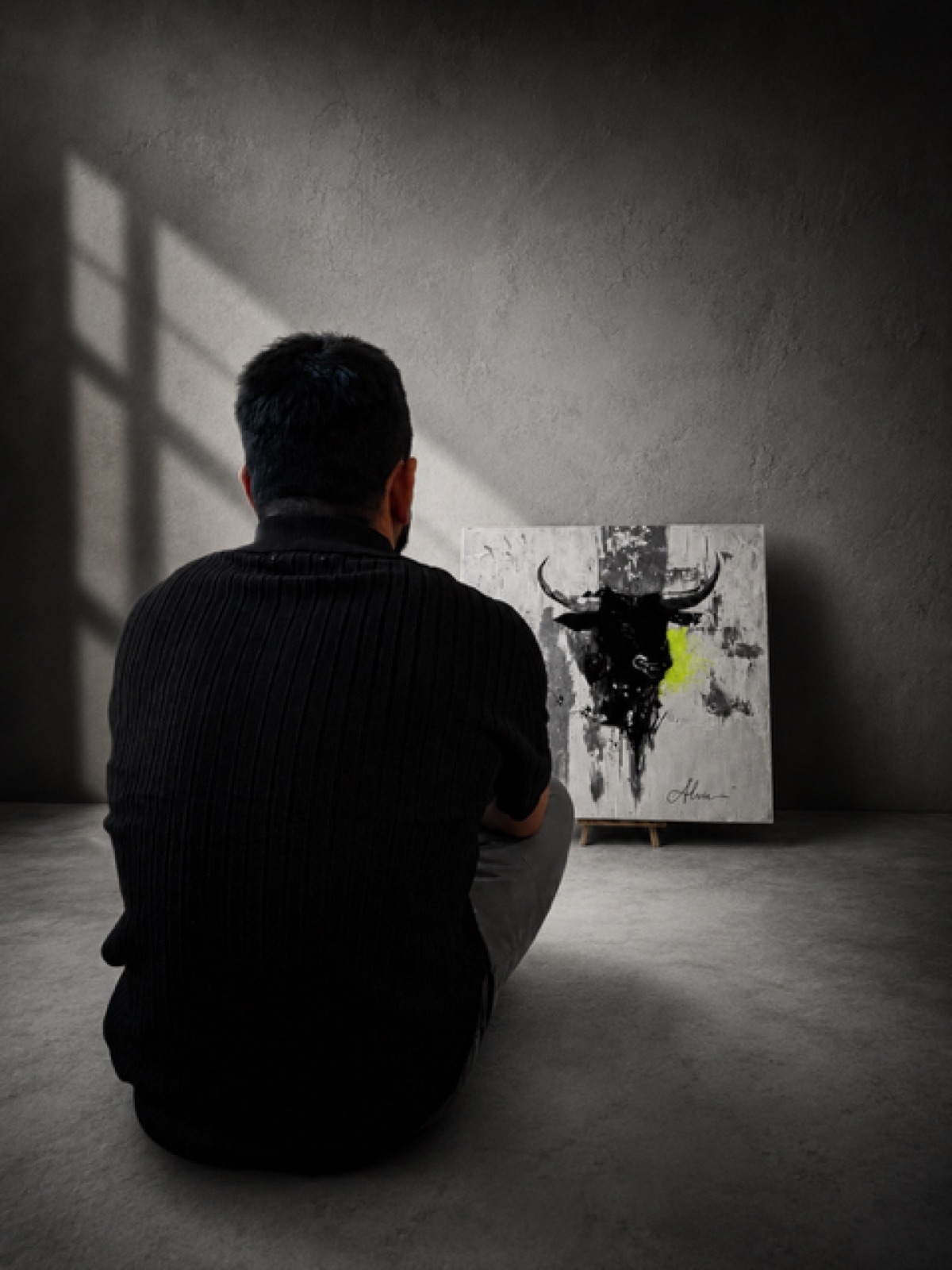The artist sitting on the floor of an empty room, looking at the painting in window light